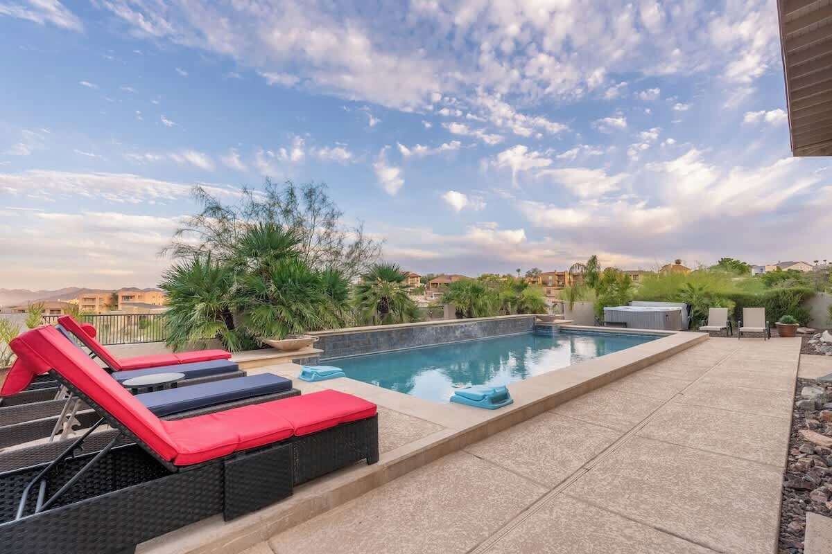 Uma piscina com espreguiçadeiras, vista para a cidade e palmeiras.
