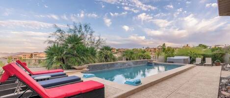 Una piscina con sillas de descanso, vistas a la ciudad y palmeras.