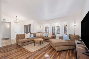 A living room with a sectional sofa, a round coffee table, and a flat-screen TV. - MountainView Estate+HeatedPool+Spa+Firepits (Fountain Hills)