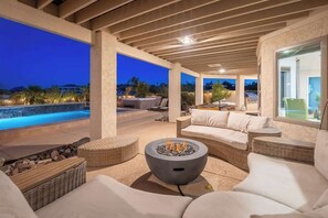 Eine Außenpatio-Terrasse mit Feuerstelle, Sitzgelegenheiten und Blick auf ein Schwimmbecken im Abenddämmerung.