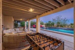 An outdoor pool area with a foosball table, a covered seating area, and a view of the pool. - MountainView Estate+HeatedPool+Spa+Firepits (Fountain Hills)