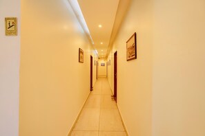 Un couloir d’hôtel avec un sol carrelé, des tableaux encadrés accrochés aux murs et un panneau indiquant les consignes de sécurité incendie.