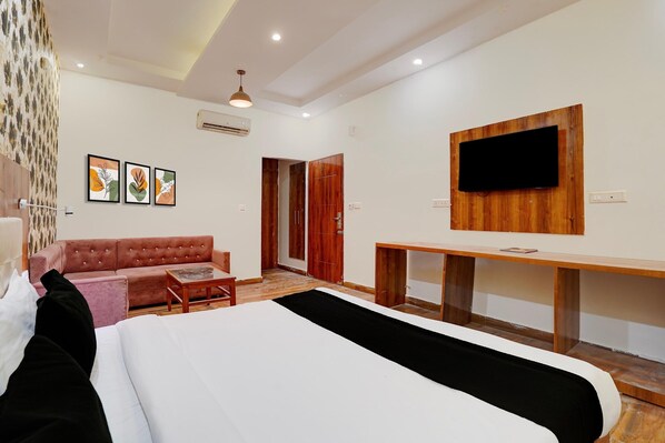 A hotel room with a bed, a sofa, a TV mounted on the wall, and a desk.