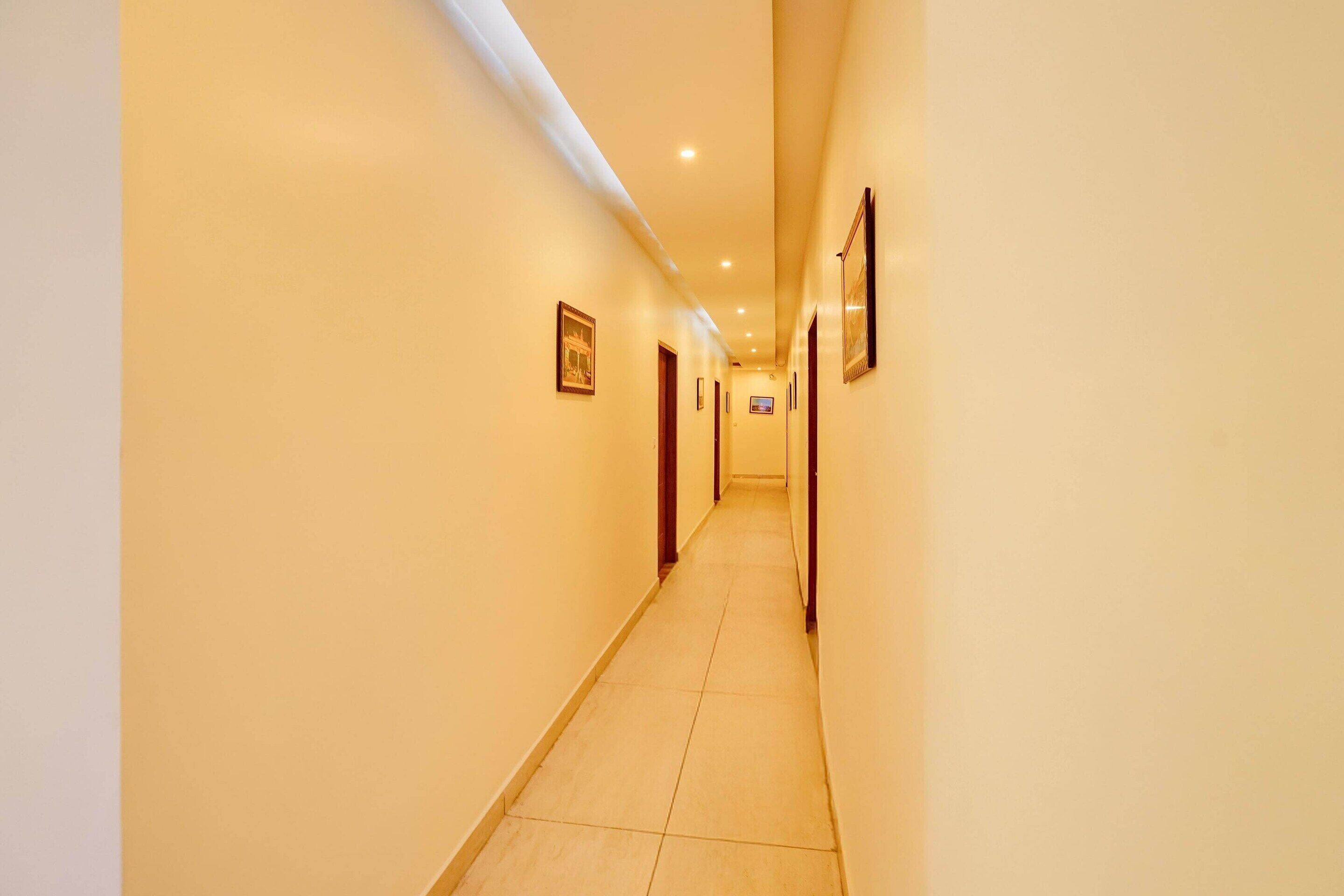 Un pasillo de hotel con puertas a ambos lados, iluminación empotrada y cuadros en las paredes.