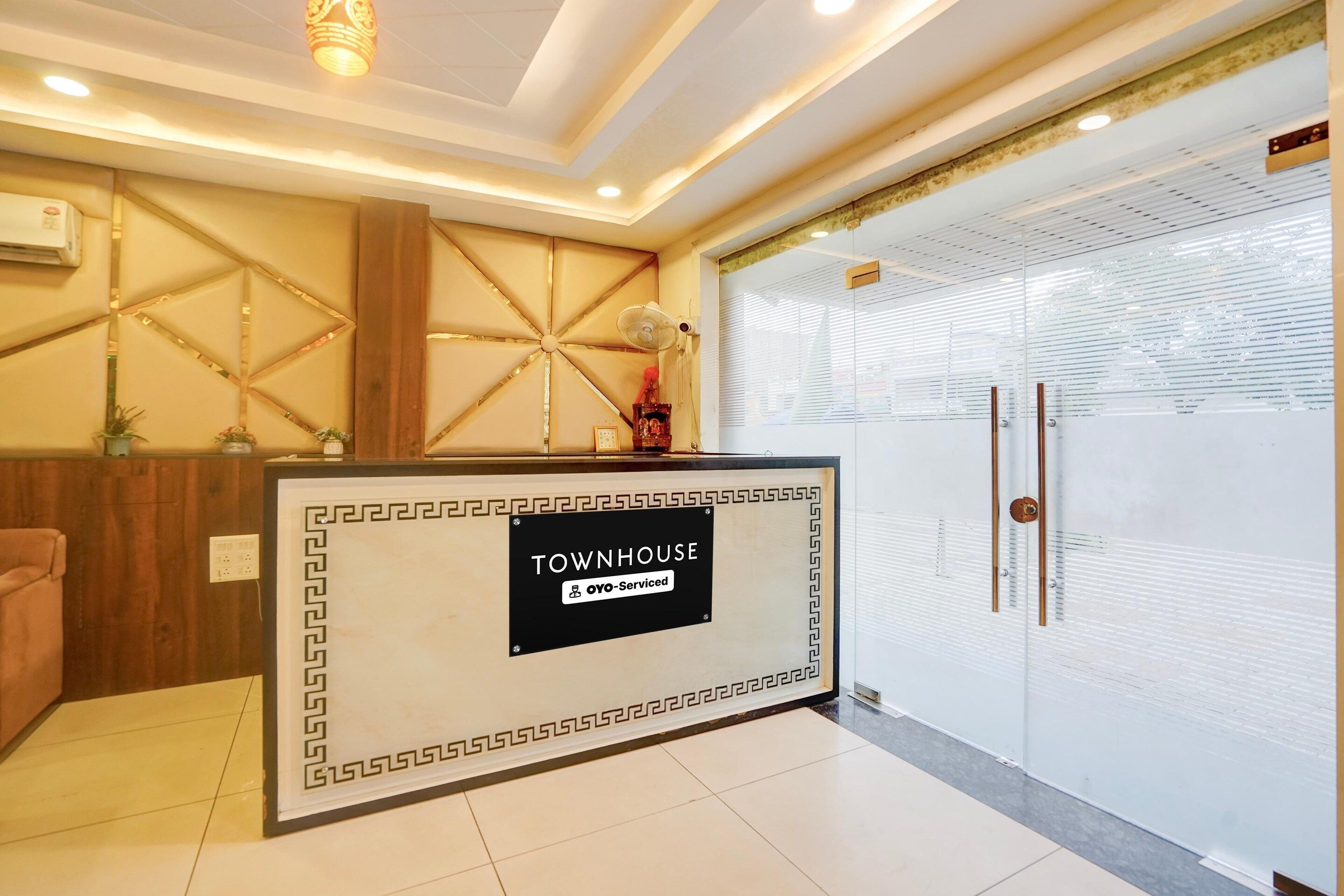 Un'area di accoglienza con una scrivania della reception, un pannello decorativo in legno, un ventilatore e una porta in vetro con motivo satinato.