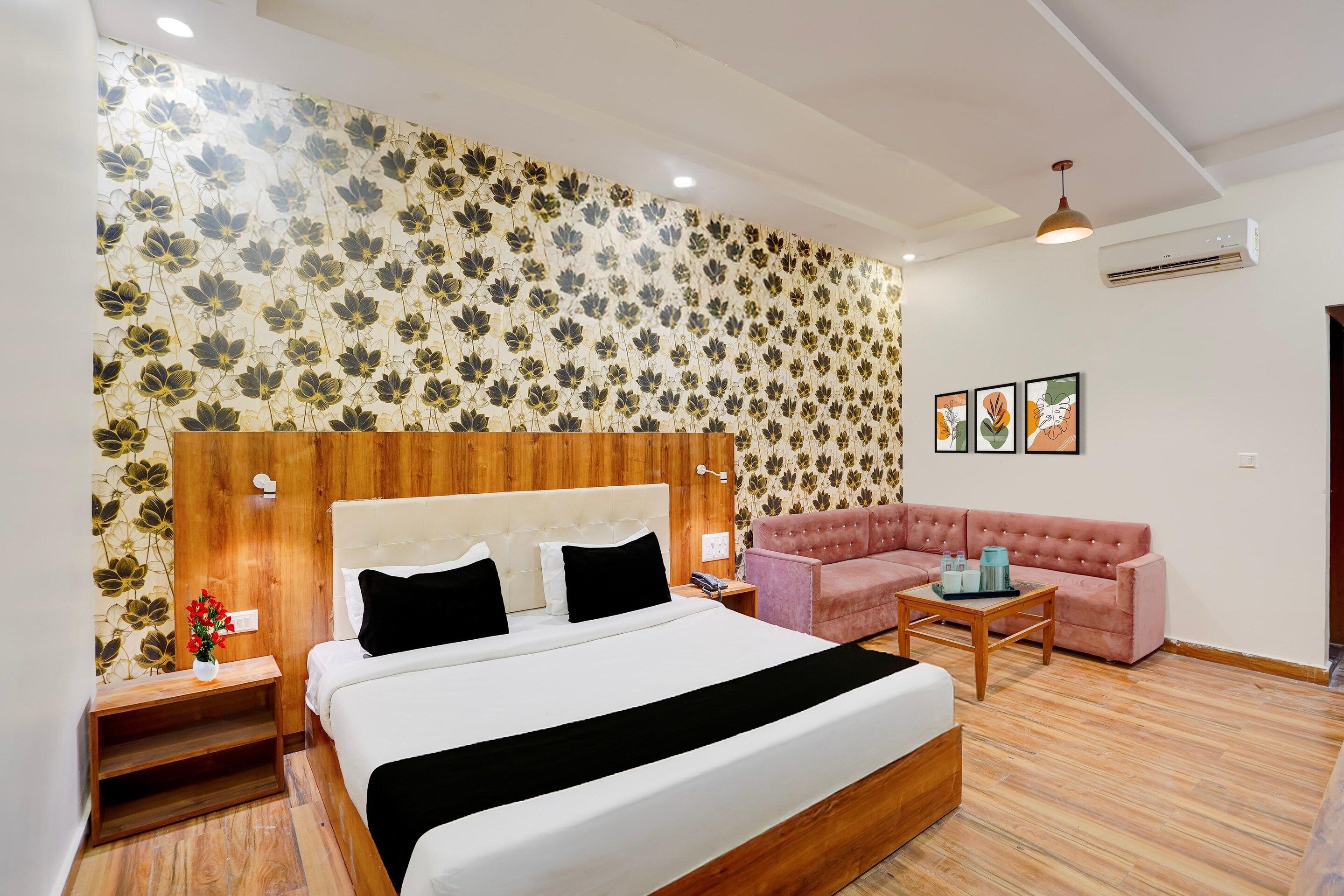 A hotel room with a bed, a sofa, a nightstand, a bedside table, and a wall with floral wallpaper.