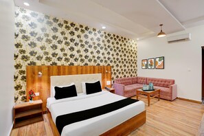 A hotel room with a bed, a sofa, a nightstand, a bedside table, and a wall with floral wallpaper.