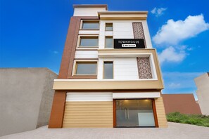 A multi-story townhouse with a garage, a sign indicating it is serviced by OYO, and a clear blue sky in the background.