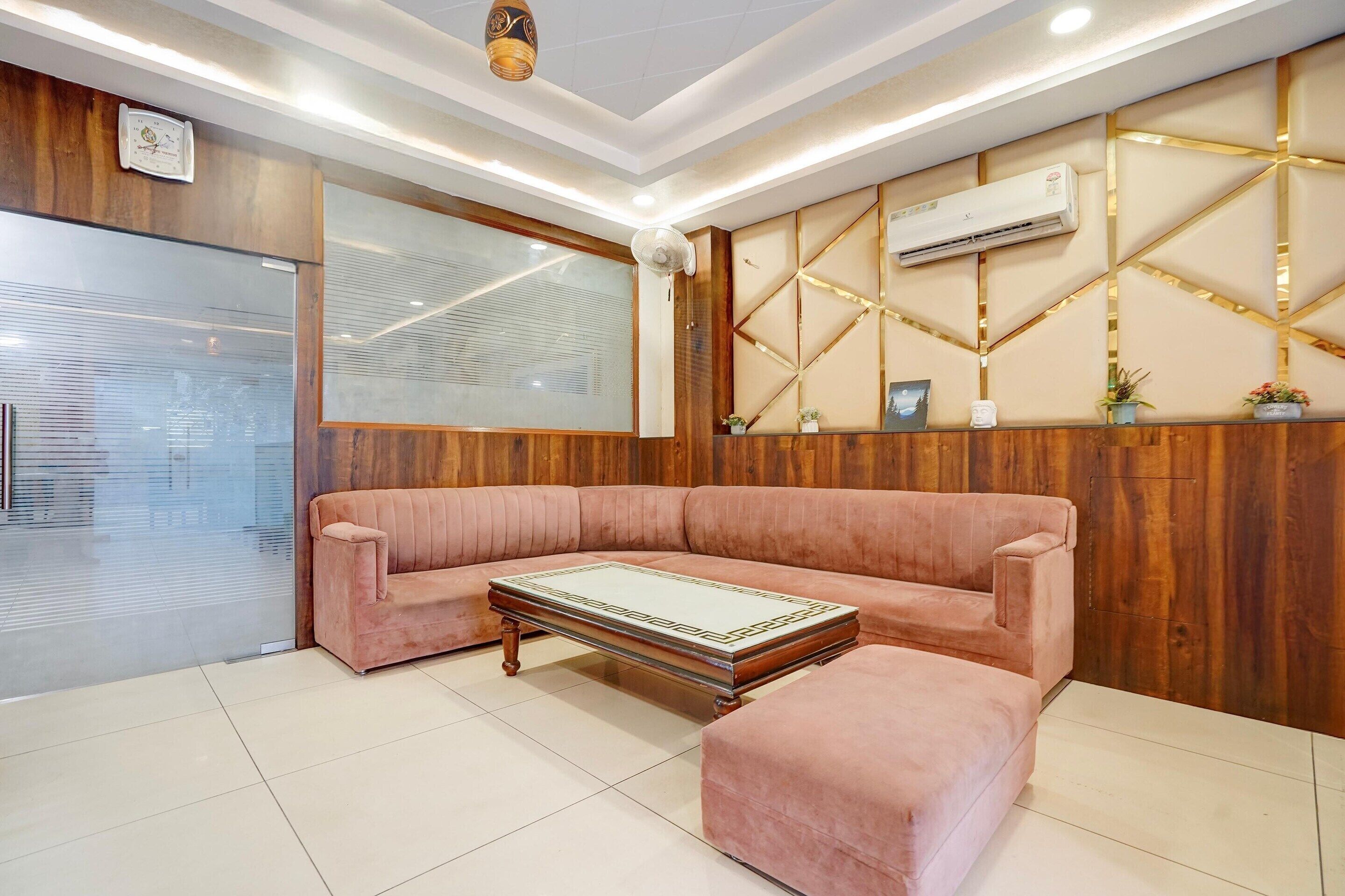 Una sala de estar moderna con un panel de madera, un sofá rosa, un reposapiés a juego y una mesa de centro de vidrio.
