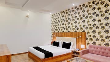 Habitación de hotel con una cama de madera, un sofá rosa, una mesa de centro de vidrio y un papel tapiz floral.