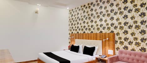 Habitación de hotel con una cama de madera, un sofá rosa, una mesa de centro de vidrio y un papel tapiz floral.