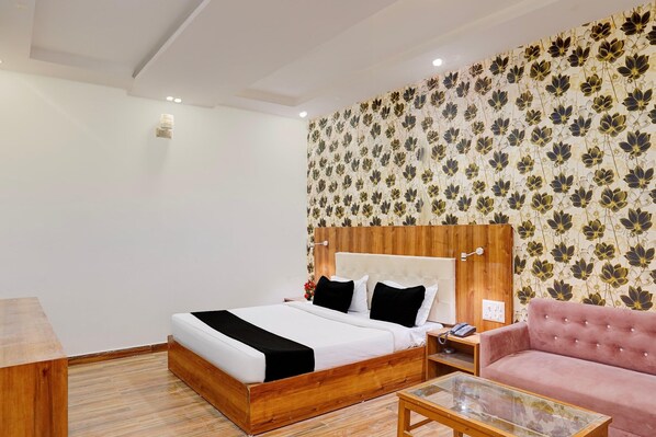 A hotel room with a wooden bed, a pink sofa, a glass coffee table, and a floral wallpaper.