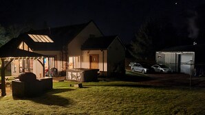 Una casa con porche cubierto, zona de barbacoa y garaje con dos coches dentro.