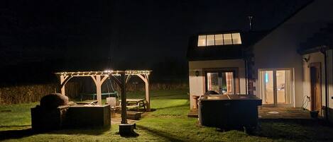A gazebo with string lights, a hot tub, and a patio area with a table and chairs.