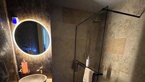Un baño moderno con un espejo redondo, un tocador de madera, cerramiento de ducha de vidrio y una toalla colgada en la pared.