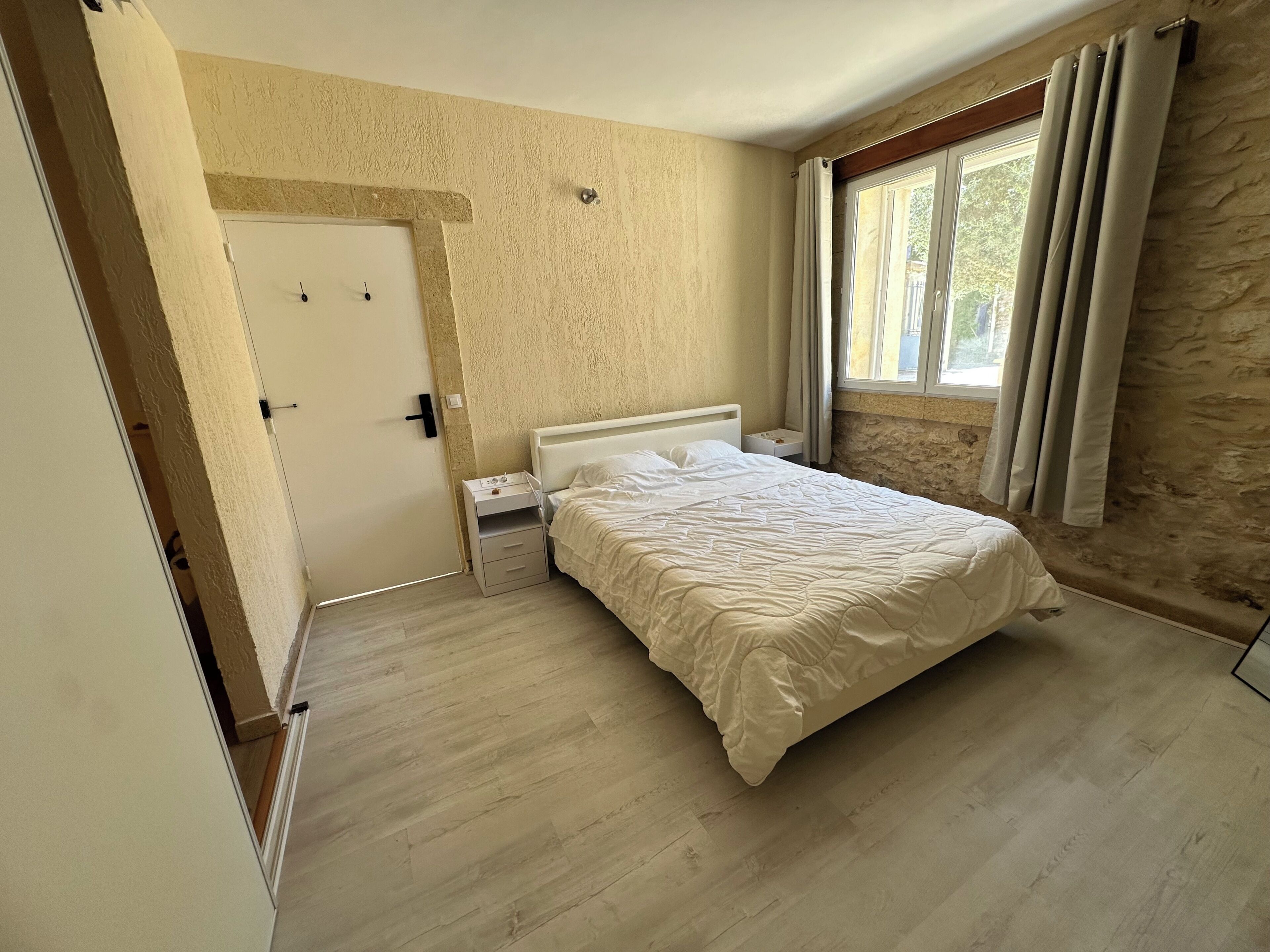 A bedroom with a bed, nightstands, a door, and a window with curtains.