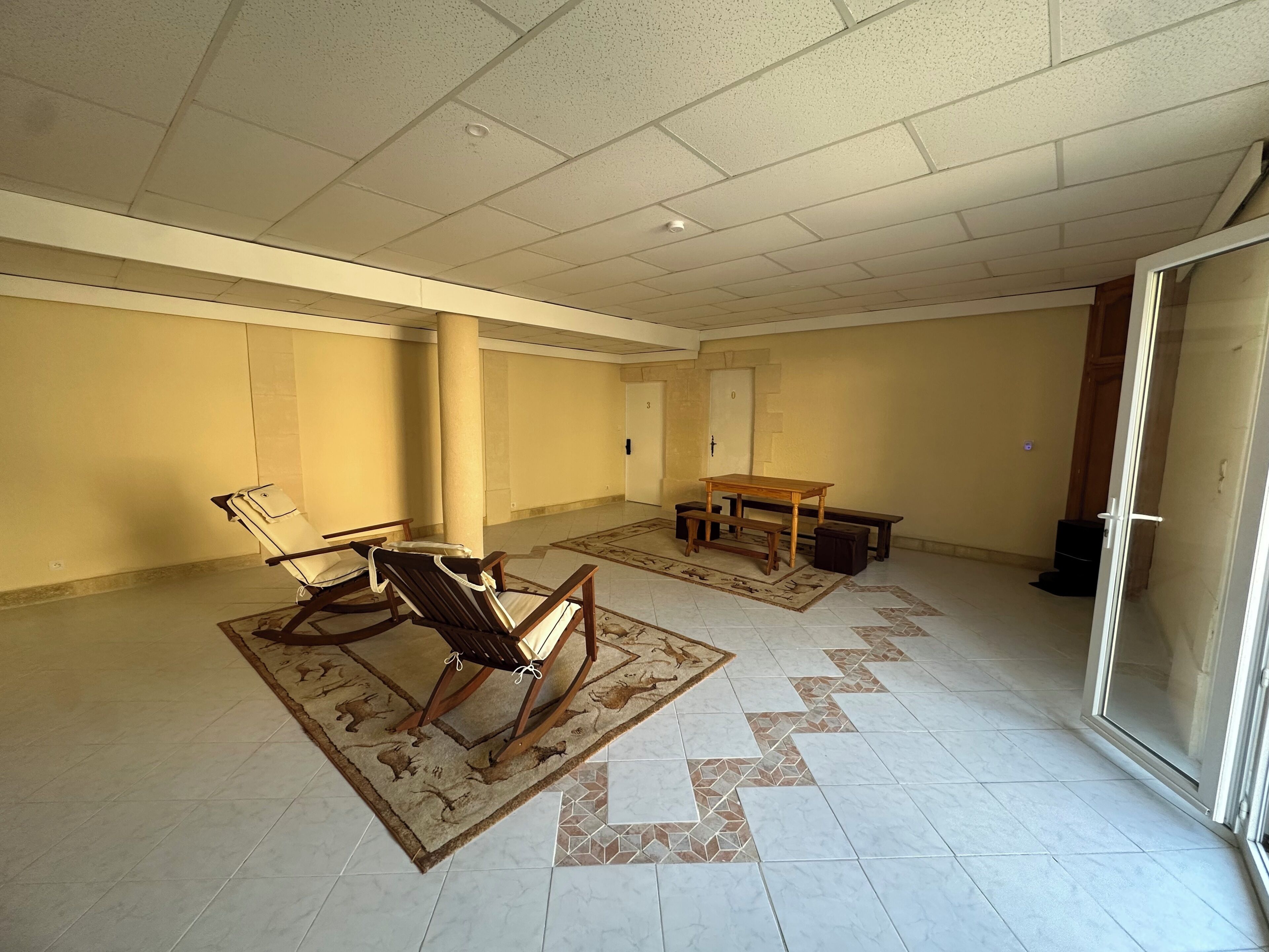 Un'ampia stanza con soffitto alto, un tavolo in legno, due sedie, una panca e un tappeto decorato.