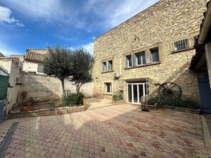 Une cour bordée de murs en pierre, avec un arbre et des plantes en pot.