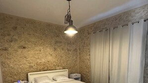 Un dormitorio con pared de piedra, una cama, una mesita de noche y una lámpara colgante.