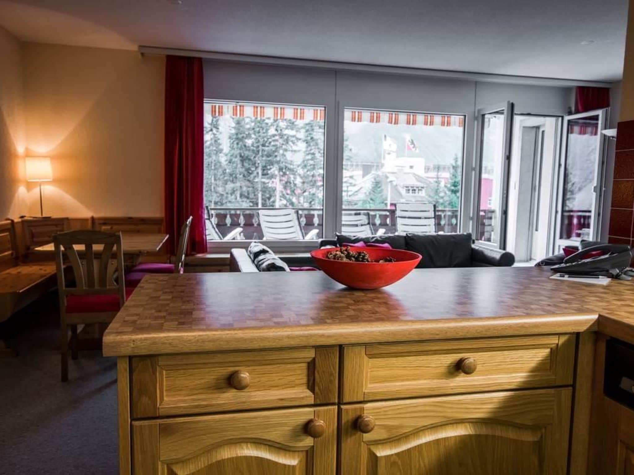 A hotel room with a wooden counter, a bowl of fruit, a sofa, and a view of the outside.
