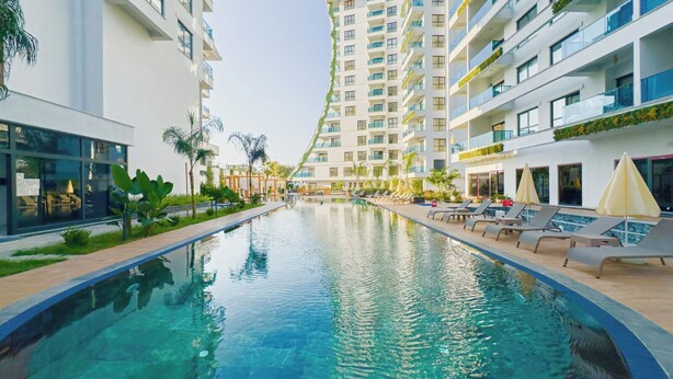 A swimming pool with lounge chairs and a modern building with balconies. - "The Best Holiday Experience in Alanya & Mahmutlar." (Mahmutlar)