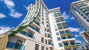 A modern high-rise building with multiple balconies, large windows, and a clear blue sky. - "The Best Holiday Experience in Alanya & Mahmutlar." (Mahmutlar)