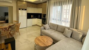 A modern living room with a sofa, round coffee table, dining area with chairs, and a kitchen in the background. - "The Best Holiday Experience in Alanya & Mahmutlar." (Mahmutlar)
