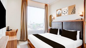 Quarto de hotel com cama grande, escrivaninha, janela com cortinas e obras de arte nas paredes.