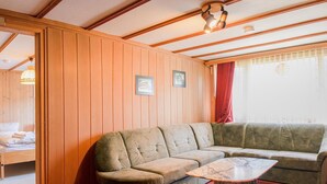 Ein gemütliches Zimmer mit einer holzverkleideten Wand, einer Couch, einem kleinen Tisch und einem Bett mit rotem Vorhang.