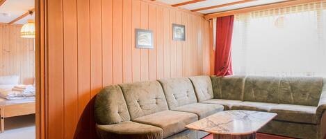 A cozy room with a wooden paneled wall, a sofa, a small table, and a bed with a red curtain.
