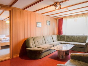 Ein gemütliches Zimmer mit einer holzverkleideten Wand, einer Couch, einem kleinen Tisch und einem Bett mit rotem Vorhang.