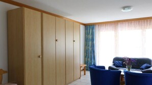 Ein Zimmer mit einem großen Kleiderschrank, einer blauen Sofagarnitur und einem kleinen Tisch mit Blumen in einer Vase.