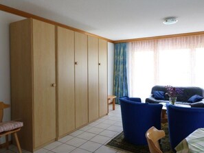 A room with a large wardrobe, a blue sofa set, and a small table with a vase of flowers. - Adlerhorst Leukerbad # 6-bed apartment, Bad, WC by Interhome (Leukerbad)