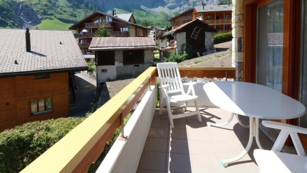 Ein Balkon mit Tisch und Stühlen, der auf eine gebirgige Landschaft mit traditionellen Häusern blickt.