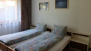 Ein Doppelbett mit gemusterten Betttextilien, ein Nachttisch und zwei gerahmte Bilder an der Wand.