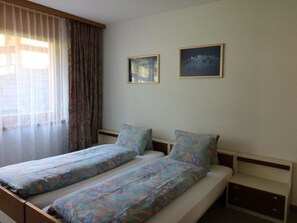 A double bed with patterned bedding, a bedside table, and two framed pictures on the wall. - Adlerhorst Leukerbad # 6-bed apartment, Bad, WC by Interhome (Leukerbad)