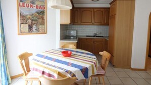 Ein Essbereich mit einem Tisch, der mit einer gestreiften Tischdecke bedeckt ist, Holzstühle, eine rote Schüssel und ein Poster an der Wand.