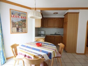 A dining area with a table covered in a striped tablecloth, wooden chairs, a red bowl, and a poster on the wall. - Adlerhorst Leukerbad # 6-bed apartment, Bad, WC by Interhome (Leukerbad)