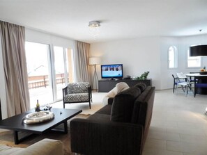 Ein modernes Wohnzimmer mit einer Couch, einem Fernseher und einem Essbereich mit Stühlen.
