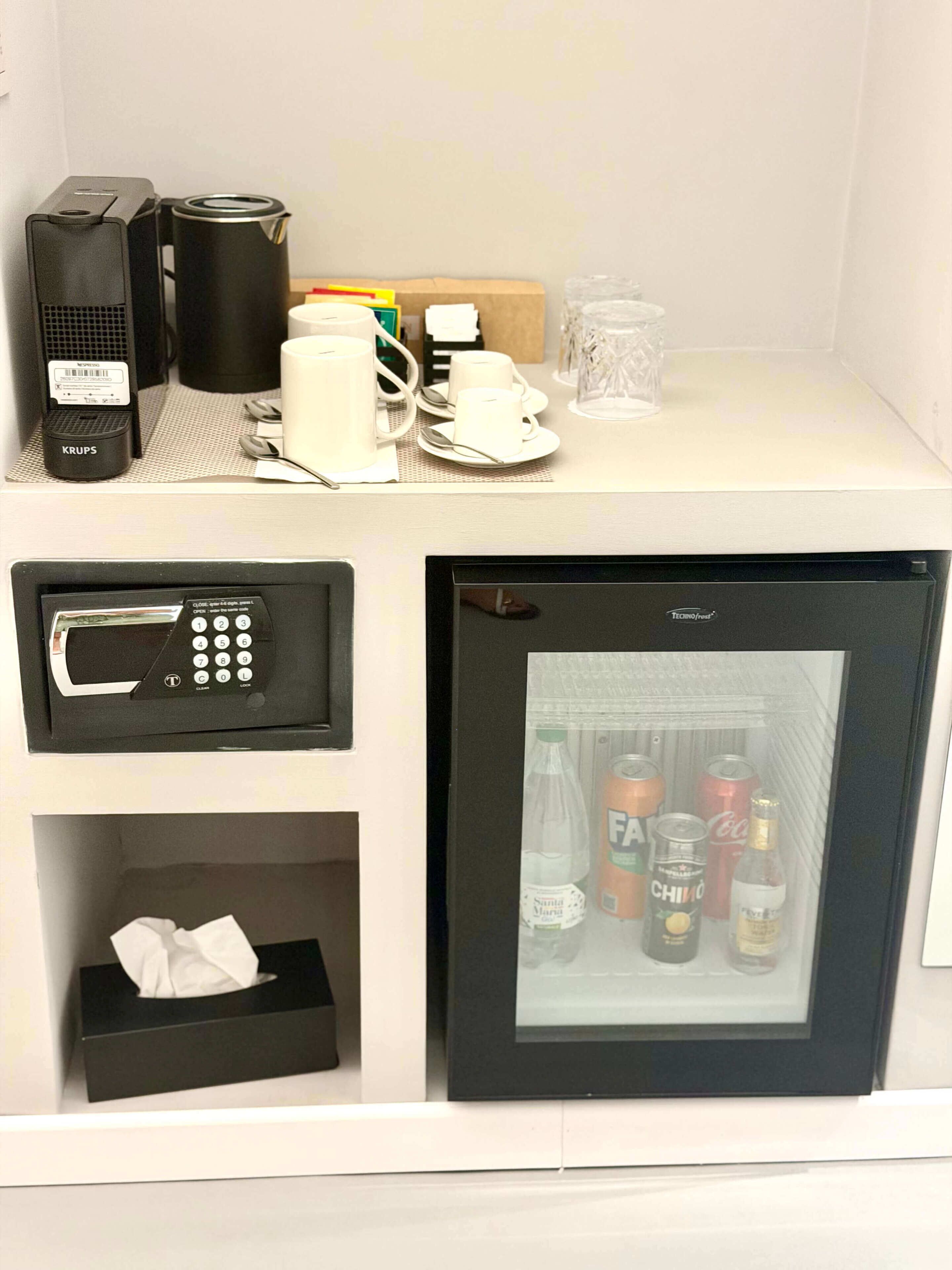 Un minibar con cafetera, microondas, refrigerador con bebidas y caja de pañuelos.