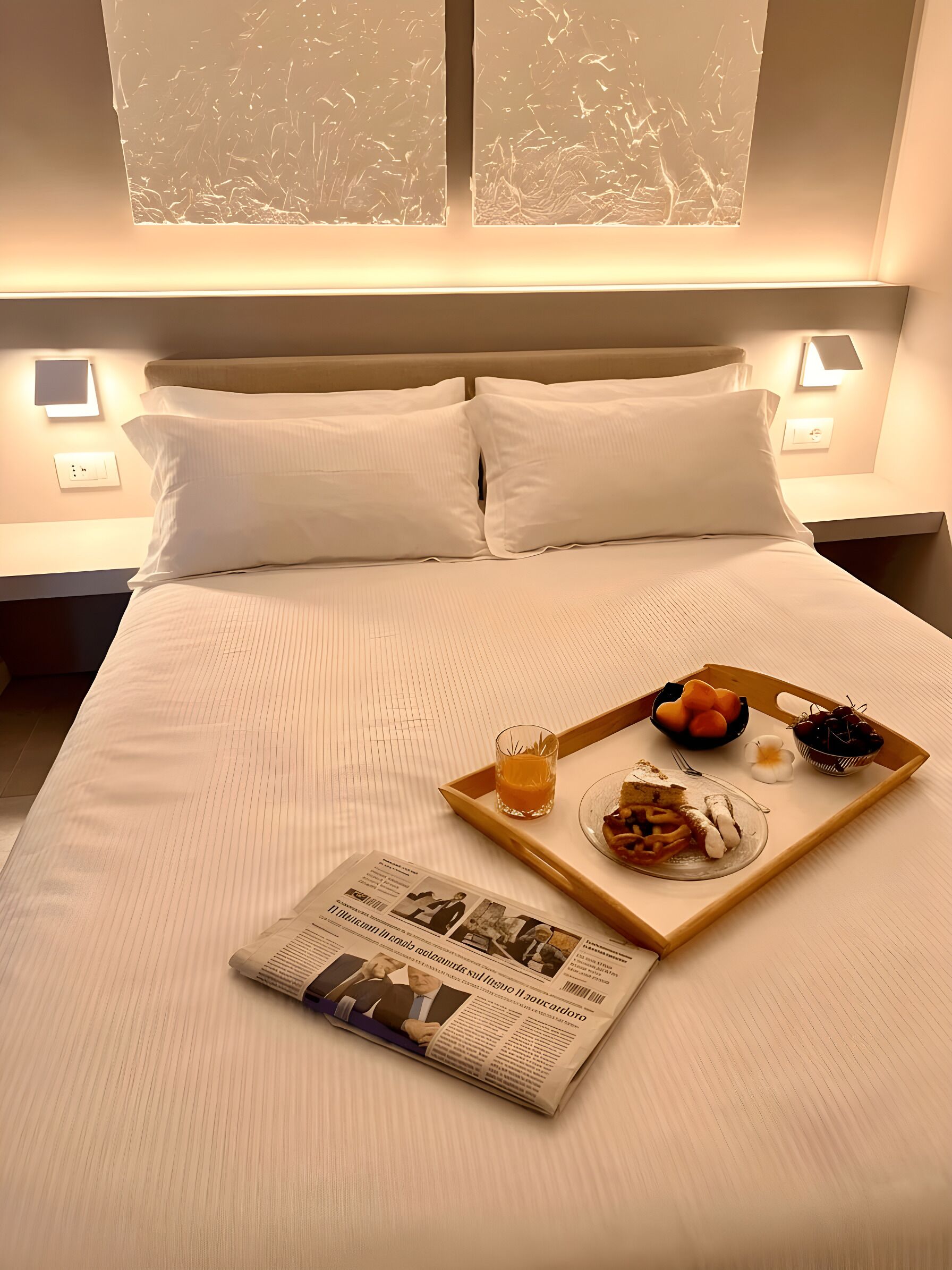 A hotel room with a neatly made bed, a tray with breakfast items, and a newspaper.
