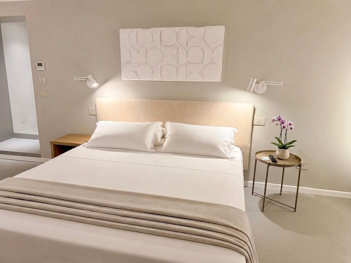 Ein modernes Hotelzimmer mit einem großen Bett, Nachttischen, einer Wandleuchte und einem kleinen Topfpflanzen.