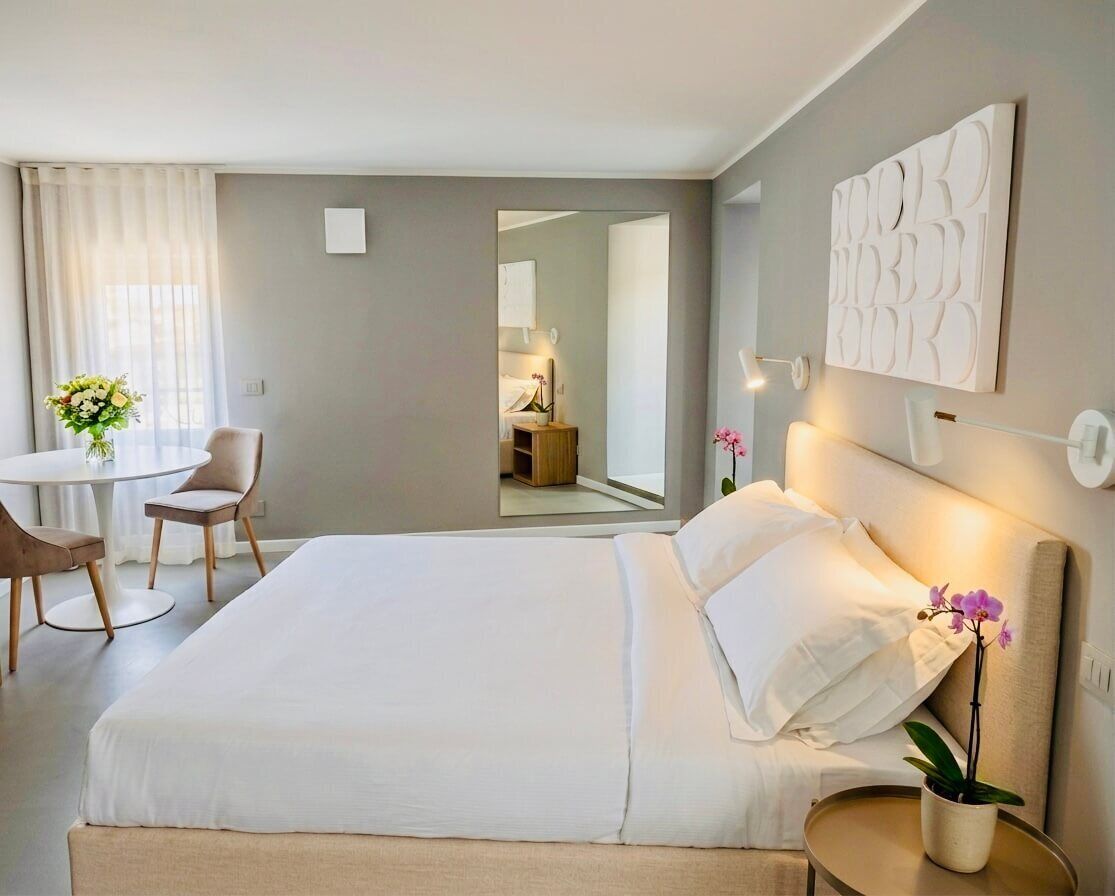 A hotel room with a bed, bedside table, lamp, and a small potted plant.