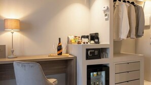 A modern hotel room with a desk, a mini-fridge, a microwave, a lamp, and a clothing rack. - DISìO DIMORA DI CHARME (Palermo)