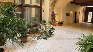 A spacious indoor courtyard with potted plants, a large window, and an arched stone structure. - DISìO DIMORA DI CHARME (Palermo)