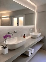 Un bagno moderno con due ampi lavandini bianchi, uno specchio e un'orchidea in vaso.