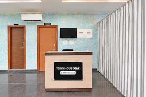 A reception desk with a sign indicating it is serviced by OYO. There are two doors, one with a sign above it, and a wall-mounted television.