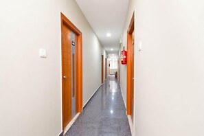 A corridor with doors on both sides, a fire extinguisher mounted on the wall, and a potted plant at the end.