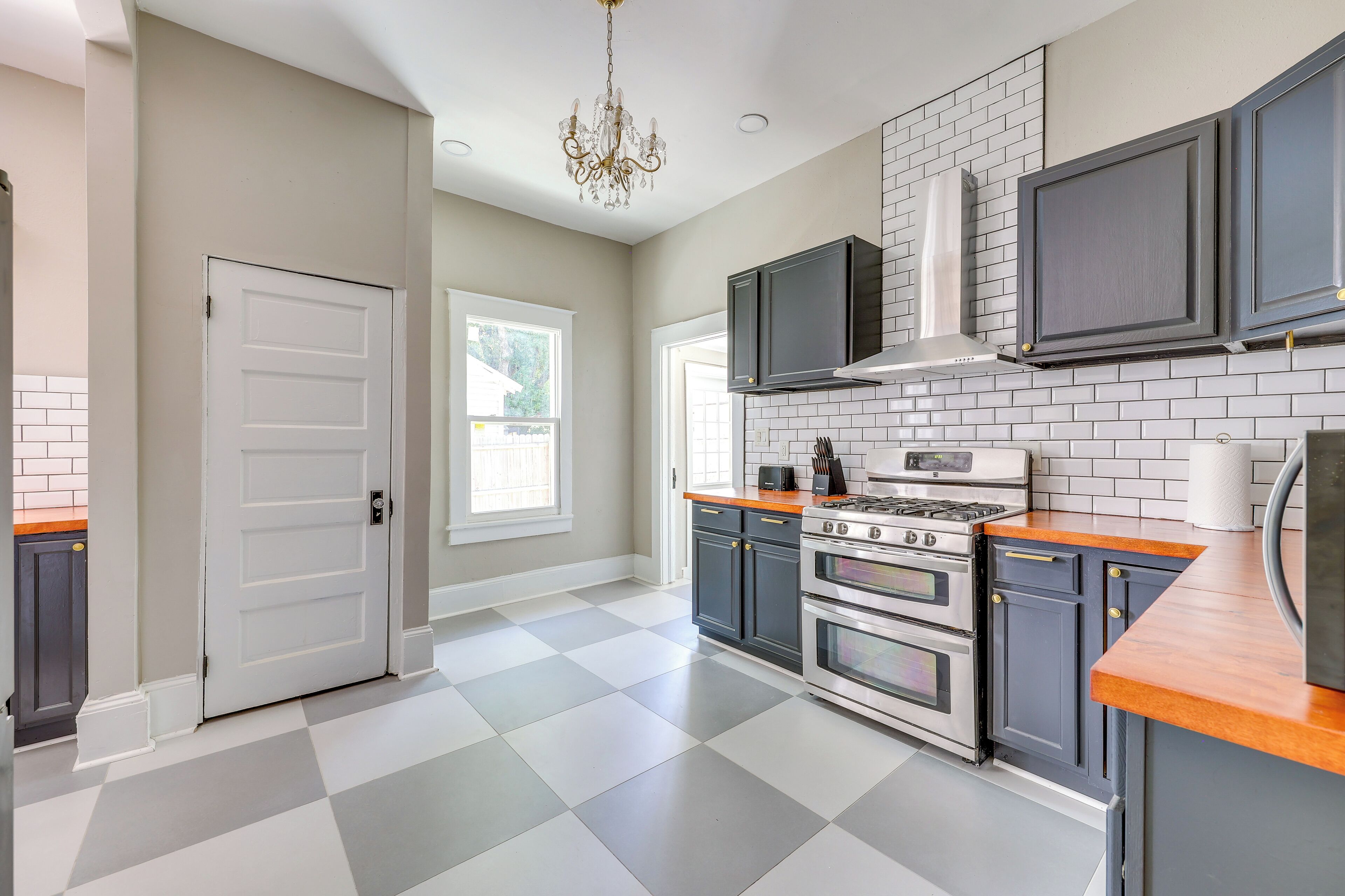 A kitchen with a checkered floor, dark cabinets, a stove, and a chandelier.