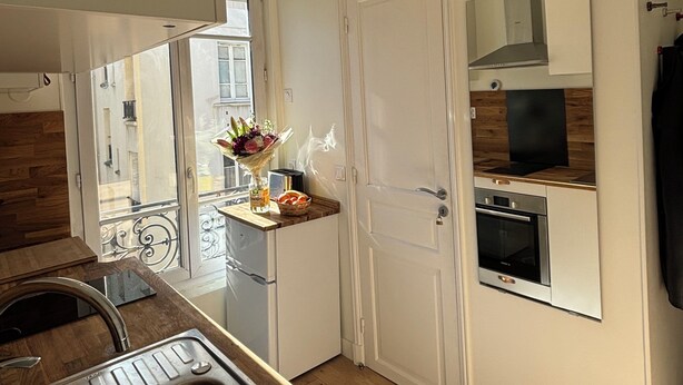 Une cuisine moderne équipée d’un four encastré, d’un évier et d’une fenêtre donnant sur un paysage urbain.